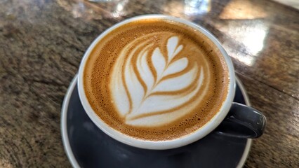 Angled top down view of beautiful flat white coffee with classic latte art in creamy frothy milk in cup and saucer on old rustic wooden table at local coffee shop
