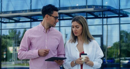 Colleagues use a tablet and talk while walking near an office building
