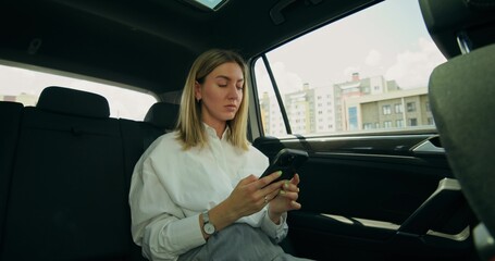 A stylish businesswoman uses a mobile phone while sitting in the back seat of a car