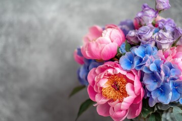 Fototapeta premium Bouquet of vibrant pink peonies eustomas and blue hydrangeas against a gray bokeh backdrop