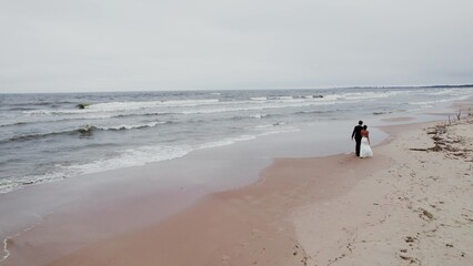 The bride and groom walk along the seashore on a windy day. View from the drone