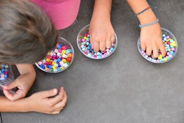 children's hands select multi-colored beads in bulk, bright balls of different shapes, craft...