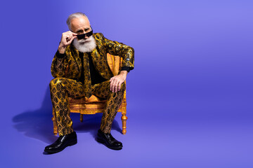 Confident elderly gentleman in an extravagant printed suit posing stylishly on a purple background...