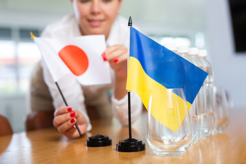 Closeup of table national flags of Ukraine and Japan in hands of female office manager preparing...