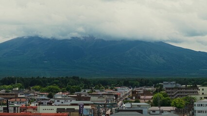 Obraz premium The city at the foot of Fujiyama. The top of the mountain is covered with clouds. Bird's-eye view of Japan's scenic nature