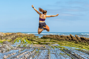 Athletic woman jumping at sakoneta beach, zumaia flysch, basque country