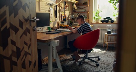 The boy is concentrating on doing his homework while sitting at the table at home