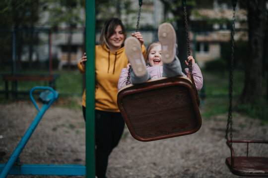 A cheerful moment of a mother pushing her happy daughter on a swing in the park. - Powered by Adobe