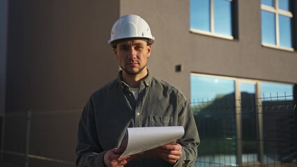 The construction engineer looks up from his notebook and smiles at the camera. He's standing outside the house.
