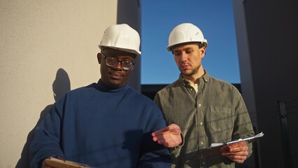 Two men in construction helmets walk past the house and discuss the details of the renovation