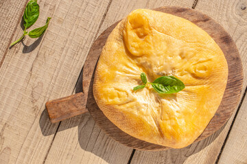 A whole smoked cheese wrapped in a natural rind garnished with a basil leaf, served on a rustic...