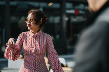A confident woman wearing sunglasses and a striped shirt is speaking assertively outdoors. The sun...