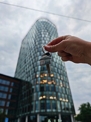 Hand holding a keychain with a house-shaped key fob and a silver key in front of a beautiful...