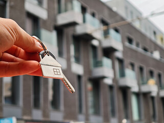 Man holding key with house-shaped keychain in front of building, symbol of new home or property