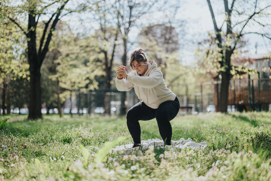 A woman wearing athletic clothing performs physical exercises in a vibrant green outdoor park. Among trees and under sunlight, she demonstrates focus and determination, embodying fitness.