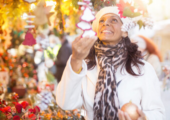Portrait of cheerful adult Latina looking for New Year decorations in traditional street market..