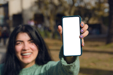 Blurry woman holding a mobile phone showing blank screen outdoors