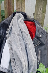 three old black leather jackets and a grey cotton one stand on the ground among green vegetation...