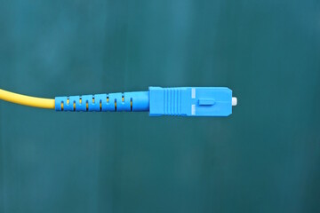 part of one yellow electrical wire with blue plastic plug on green background