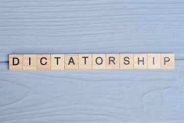 text the word dictatorship from wooden small letters with black font on an gray table