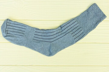one gray long fabric sock lies on a yellow wooden table in the room