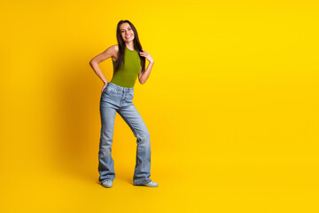 Cheerful woman in casual khaki top and jeans posing confidently against a vibrant yellow background...