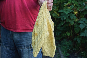 one man holding small wool knitted yellow sweater in hand on summer street