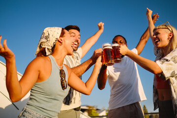 Friends toasting with beer mugs at rooftop party, celebrating friendship
