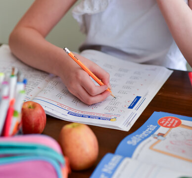 A young girl focuses on solving math problems in her workbook during a homeschool lesson. Ideal for concepts of homeschooling, independent learning, and early education.