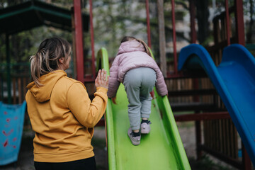 Obraz premium A mother supports her daughter as she climbs a slide at a vibrant park playground, showcasing fun and care. The image reflects family love, encouragement, and outdoor recreational activities.