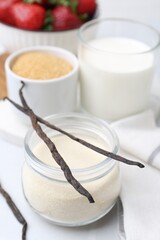 Different ingredients for panna cotta. Milk, sugar, vanilla and strawberries on white tiled table, closeup
