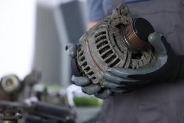 Auto parts. Professional mechanic with alternator near indoors, closeup. Space for text