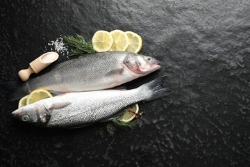 Fresh raw seabass fish with spices on black table, flat lay and space for text. Seafood delicacies