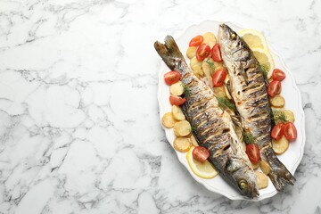 Tasty roasted seabass fish served with potatoes, tomatoes and lemon on white marble table, top view and space for text. Homemade seafood dish