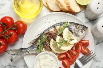 Tasty roasted dorado fish with bread, sauce, tomatoes and lemon on white marble table, flat lay. Homemade seafood dish