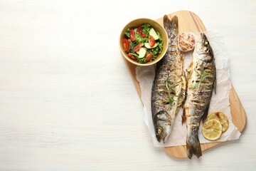 Tasty roasted seabass fish served with salad and lemon on white wooden table, top view and space for text. Homemade seafood dish