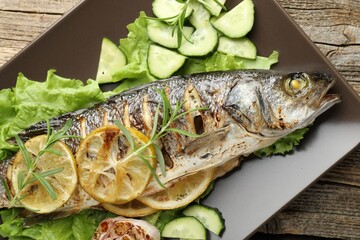 Tasty roasted seabass fish served with vegetables and lemon on wooden table, top view. Homemade seafood dish
