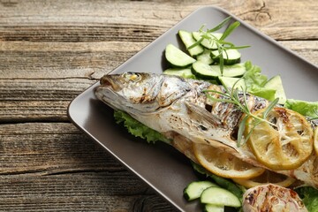 Tasty roasted seabass fish served with vegetables and lemon on wooden table, closeup. Homemade seafood dish