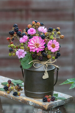 Blumenstrau&szlig; mit pink Zinnien, Federnelken und Brombeerzweigen im alten Milchkrug