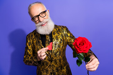 Stylish senior man in a golden snake print suit holding a rose and red heart on a vibrant purple...