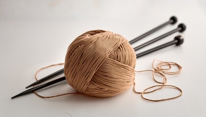 tan yarn ball with knitting needles and black thread on white craft hobby