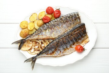 Tasty roasted mackerels with lemon, tomatoes and potatoes on white wooden table, top view. Homemade seafood dish