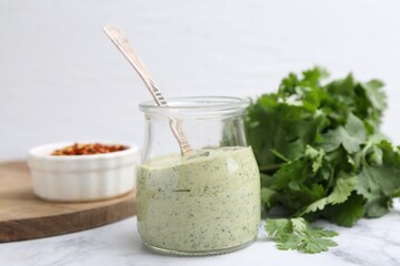 Tasty cilantro sauce and spoon in jar on light marble table, closeup