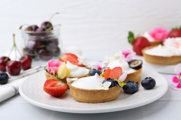 Delicious dessert. Tartlets with cream, berries and flowers on white tiled table, closeup