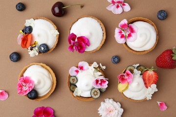 Delicious dessert. Tartlets with cream, berries and flowers on light brown background, flat lay