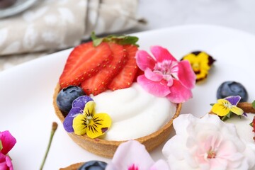 Sweet tartlets with berries and flowers on light table, closeup. Delicious dessert