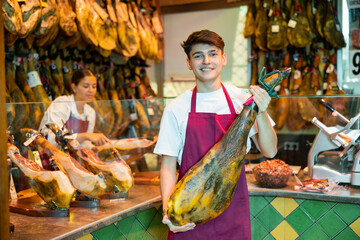 Smiling seller offering delectable spanish jamon in butcher shop