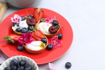 Sweet tartlets with berries and flowers on light grey table, closeup with space for text. Delicious...