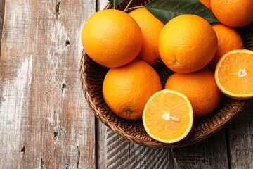 Fresh oranges and leaves in wicker basket on wooden table, top view. Space for text