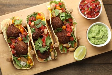 Tasty vegetarian tacos with falafel served with salsa and guacamole on wooden table, top view